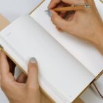 Person writing daily habits in a notebook for habits to track